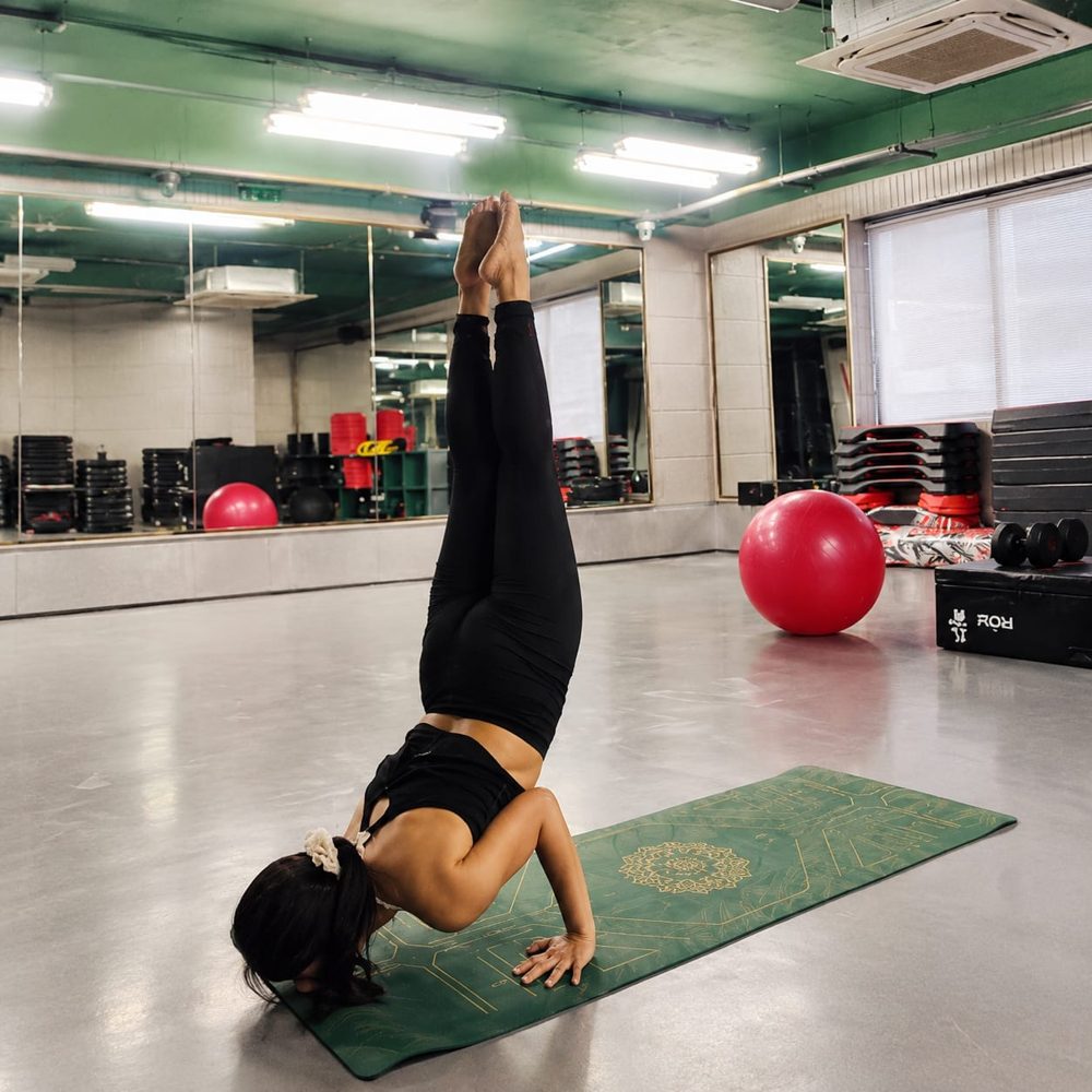 Sakshi holding a forearm stand on a green yoga mat